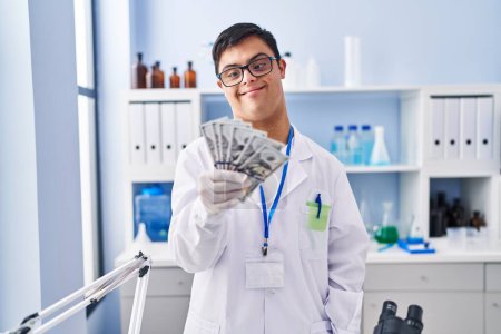 Téléchargez les photos : Homme trisomique portant l'uniforme de scientifique tenant des dollars au laboratoire - en image libre de droit