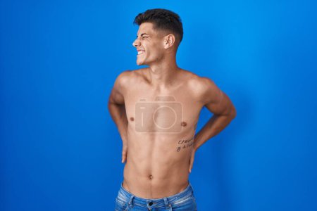 Photo for Young hispanic man standing shirtless over blue background suffering of neck ache injury, touching neck with hand, muscular pain - Royalty Free Image