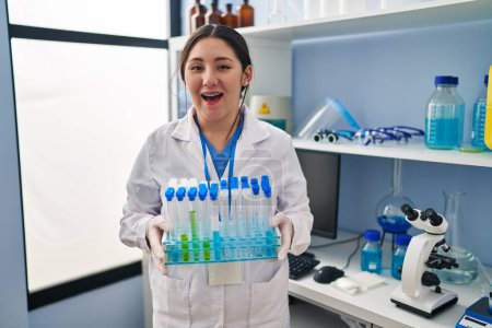 Photo for Young latin woman working at scientist laboratory smiling and laughing hard out loud because funny crazy joke. - Royalty Free Image