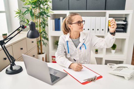 Téléchargez les photos : Young blonde woman wearing doctor uniform prescribe pills at clinic - en image libre de droit