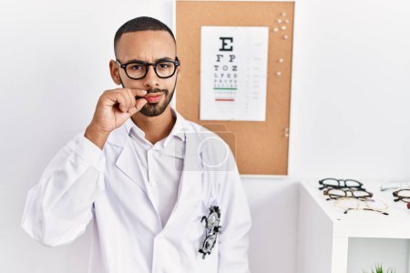 Photo for African american optician man standing by eyesight test mouth and lips shut as zip with fingers. secret and silent, taboo talking - Royalty Free Image