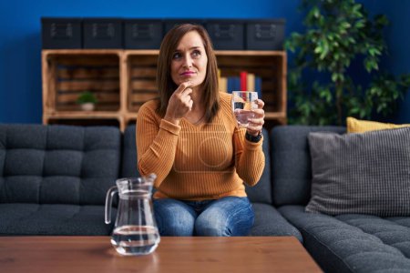 Photo for Middle age woman drinking glass of water serious face thinking about question with hand on chin, thoughtful about confusing idea - Royalty Free Image