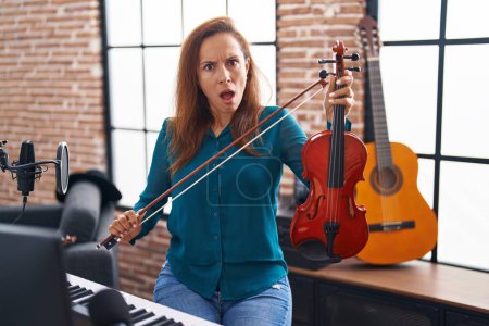Photo for Brunette woman playing violin in shock face, looking skeptical and sarcastic, surprised with open mouth - Royalty Free Image