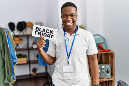 Foto de Joven africano sosteniendo el estandarte del viernes negro en la tienda minorista luciendo positivo y feliz de pie y sonriendo con una sonrisa confiada mostrando los dientes - Imagen libre de derechos