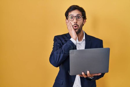 Photo for Handsome latin man working using computer laptop afraid and shocked, surprise and amazed expression with hands on face - Royalty Free Image