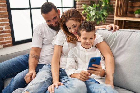Photo for Family using smartphone hugging each other sitting on sofa at home - Royalty Free Image