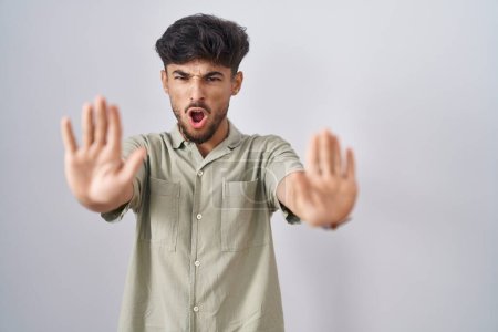 Téléchargez les photos : Homme arabe avec barbe debout sur fond blanc faisant geste d'arrêt avec les mains paumes de la main, expression de colère et de frustration - en image libre de droit