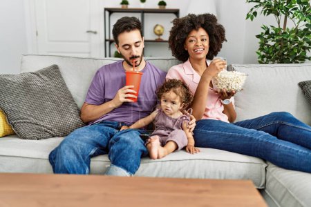 Téléchargez les photos : Couple and daughter watching movie sitting on sofa at home - en image libre de droit