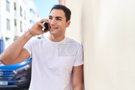 Téléchargez les photos : Jeune homme hispanique souriant confiant parler sur le smartphone à la rue - en image libre de droit