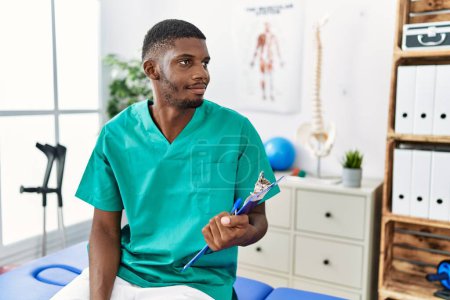 Téléchargez les photos : Young african american man working at pain recovery clinic looking to side, relax profile pose with natural face and confident smile. - en image libre de droit