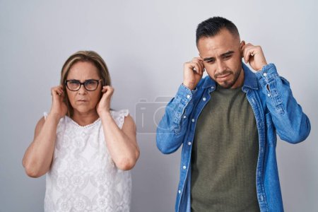 Téléchargez les photos : Hispanic mother and son standing together covering ears with fingers with annoyed expression for the noise of loud music. deaf concept. - en image libre de droit