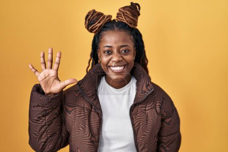 Téléchargez les photos : African woman with braided hair standing over yellow background showing and pointing up with fingers number five while smiling confident and happy. - en image libre de droit