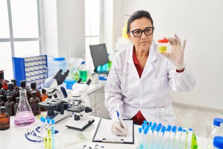 Téléchargez les photos : Middle age hispanic woman wearing scientist uniform analysing urine test at laboratory - en image libre de droit