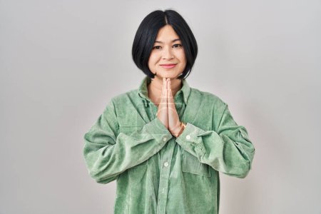 Téléchargez les photos : Jeune femme asiatique debout sur fond blanc priant avec les mains ensemble demandant pardon souriant confiant. - en image libre de droit