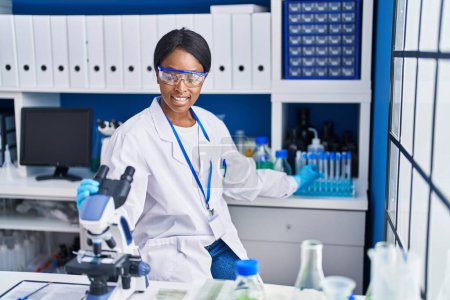Photo for Young african american woman scientist using microscope working at laboratory - Royalty Free Image