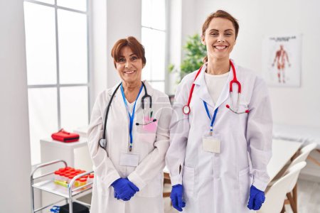 Photo for Two women wearing doctor uniform and stethoscope looking positive and happy standing and smiling with a confident smile showing teeth - Royalty Free Image