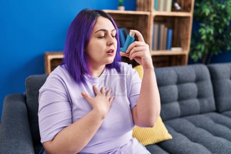 Photo for Young beautiful plus size woman using inhaler sitting on sofa at home - Royalty Free Image