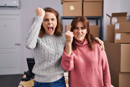 Photo for Two women working at small business ecommerce annoyed and frustrated shouting with anger, yelling crazy with anger and hand raised - Royalty Free Image