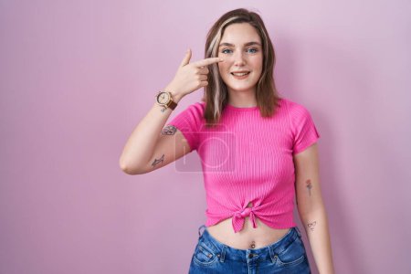 Photo for Blonde caucasian woman standing over pink background pointing with hand finger to face and nose, smiling cheerful. beauty concept - Royalty Free Image