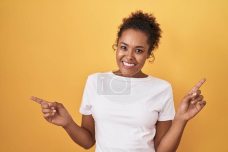 Téléchargez les photos : Young hispanic woman with curly hair standing over yellow background smiling confident pointing with fingers to different directions. copy space for advertisement - en image libre de droit
