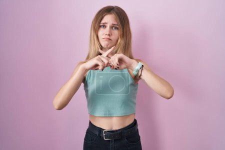 Photo for Blonde caucasian woman standing over pink background rejection expression crossing fingers doing negative sign - Royalty Free Image