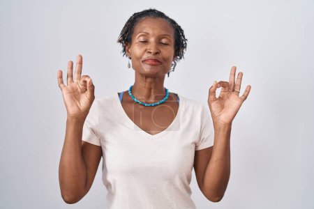 Téléchargez les photos : Femme africaine avec dreadlocks debout sur fond blanc se détendre et sourire avec les yeux fermés faire geste de méditation avec les doigts. concept de yoga. - en image libre de droit