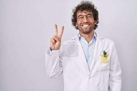 Téléchargez les photos : Jeune homme hispanique portant l'uniforme de médecin montrant et pointant vers le haut avec les doigts numéro deux tout en souriant confiant et heureux. - en image libre de droit
