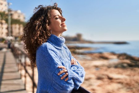 Photo for Young hispanic woman smiling confident breathing with arms crossed gesture at seaside - Royalty Free Image