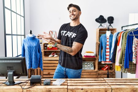 Téléchargez les photos : Jeune homme hispanique travaillant à la boutique de détail pointant de côté avec les mains ouvertes paumes montrant l'espace de copie, présentant la publicité souriant heureux heureux - en image libre de droit
