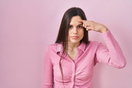 Téléchargez les photos : Jeune femme hispanique debout sur fond rose pointant malheureux à boutons sur le front, infection laide de la tête noire. acné et problème de peau - en image libre de droit
