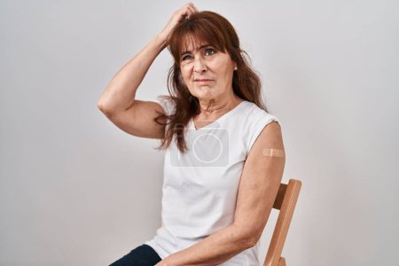 Photo for Middle age hispanic woman getting vaccine showing arm with band aid confuse and wondering about question. uncertain with doubt, thinking with hand on head. pensive concept. - Royalty Free Image