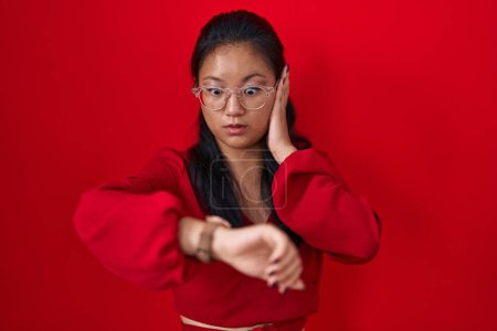 Téléchargez les photos : Asiatique jeune femme debout sur fond rouge regardant le temps de la montre inquiet, peur de se faire tard - en image libre de droit