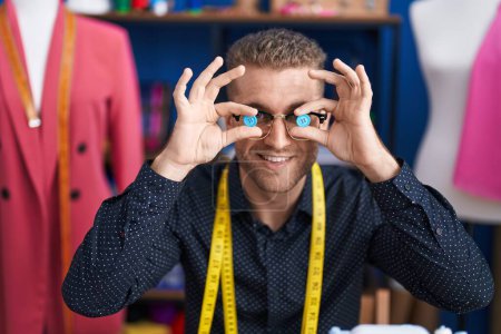 Téléchargez les photos : Young caucasian man tailor smiling confident holding buttons over eyes at clothing factory - en image libre de droit