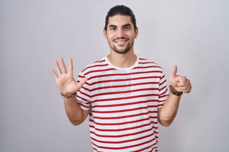 Téléchargez les photos : Hispanic man with long hair standing over isolated background showing and pointing up with fingers number six while smiling confident and happy. - en image libre de droit