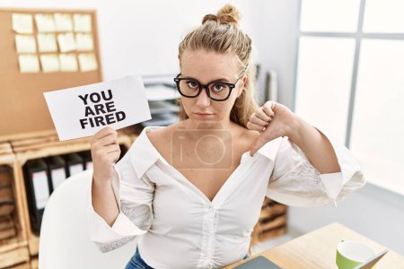 Photo for Young caucasian woman holding you are fired banner at the office with angry face, negative sign showing dislike with thumbs down, rejection concept - Royalty Free Image