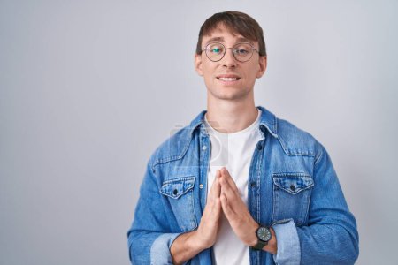 Téléchargez les photos : Caucasian blond man standing wearing glasses hands together and fingers crossed smiling relaxed and cheerful. success and optimistic - en image libre de droit