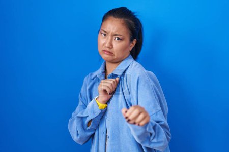 Photo for Asian young woman standing over blue background disgusted expression, displeased and fearful doing disgust face because aversion reaction. - Royalty Free Image
