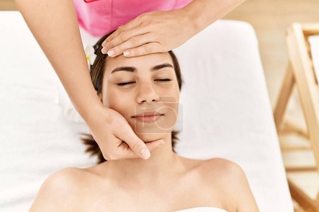Téléchargez les photos : Jeune femme hispanique souriante confiante ayant massage facial au centre de beauté. - en image libre de droit