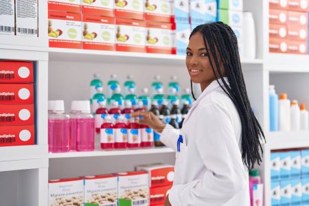 Téléchargez les photos : African american woman pharmacist smiling confident organizing shelving at pharmacy - en image libre de droit