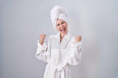 Téléchargez les photos : Femme caucasienne blonde portant un peignoir très heureux et excité faisant geste gagnant avec les bras levés, souriant et criant pour le succès. concept de célébration. - en image libre de droit