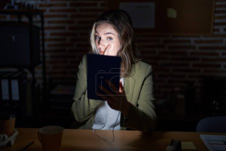 Photo for Blonde caucasian woman working at the office at night pointing to the eye watching you gesture, suspicious expression - Royalty Free Image