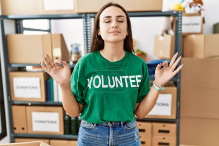 Photo for Young brunette woman wearing volunteer t shirt at donations stand relaxed and smiling with eyes closed doing meditation gesture with fingers. yoga concept. - Royalty Free Image