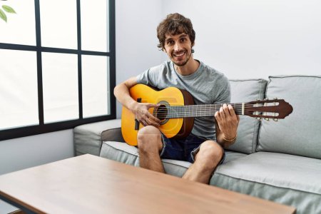 Photo for Young hispanic man smiling confident playing classical guitar at home - Royalty Free Image