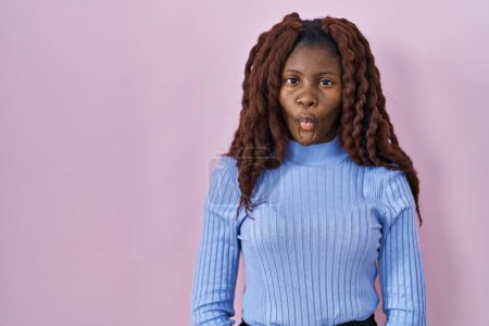 Foto de African woman standing over pink background making fish face with lips, crazy and comical gesture. funny expression. - Imagen libre de derechos