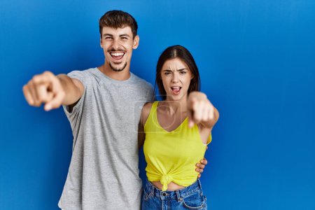 Photo for Young hispanic couple standing together over blue background pointing displeased and frustrated to the camera, angry and furious with you - Royalty Free Image