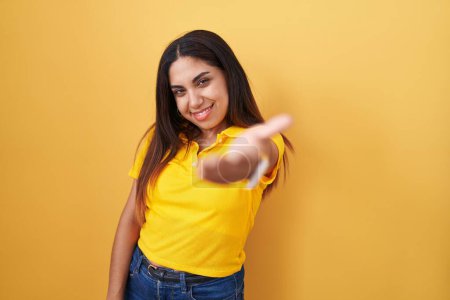 Téléchargez les photos : Jeune femme arabe debout sur fond jaune souriant joyeuse offrant main de paume donnant assistance et acceptation. - en image libre de droit