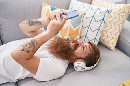 Photo for Young redhead man listening to music lying on sofa at home - Royalty Free Image