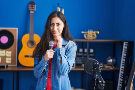 Photo for Young teenager girl singing song using microphone serious face thinking about question with hand on chin, thoughtful about confusing idea - Royalty Free Image