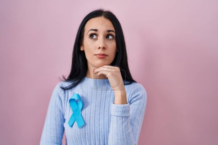 Photo for Hispanic woman wearing blue ribbon serious face thinking about question with hand on chin, thoughtful about confusing idea - Royalty Free Image