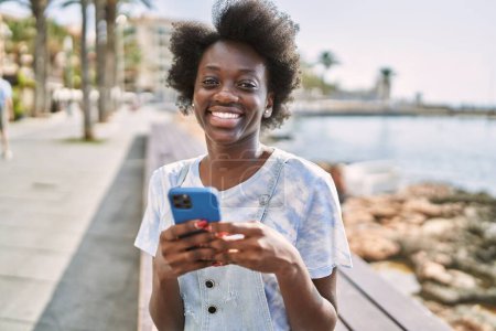 Téléchargez les photos : Jeune femme africaine utilisant un smartphone au bord de la mer - en image libre de droit